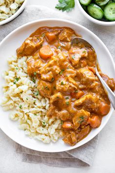 a white plate topped with rice and meat covered in gravy next to bowls of cucumbers