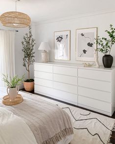 a bedroom with white furniture and plants in vases on top of the dresser next to it