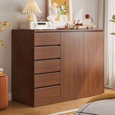 a brown dresser with drawers and pictures on it in a room next to a window