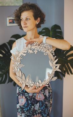 a woman holding a mirror with flowers on it in front of a potted plant