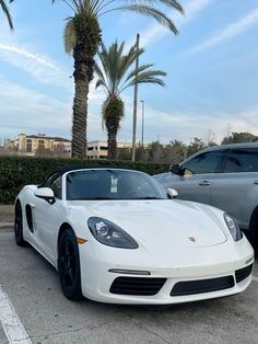 a white sports car parked in a parking lot next to two other cars and palm trees