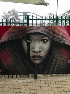 a woman's face is painted on the side of a fence in front of a building