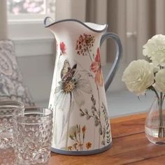 a pitcher and glasses on a table with flowers in vases next to the pitcher