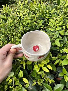 someone is holding a coffee cup in front of some bushes and trees with a cherry on it