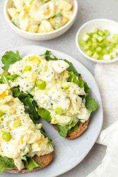 an open face sandwich on a white plate with green onions and cucumber in the background