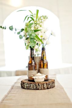 two beer bottles with flowers in them sitting on a piece of burlocked wood