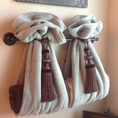 two white towels hanging on the wall with tassels attached to them and one has a brown handle