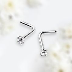 two silver nose piercings with white flowers in the background, one is shaped like an ear