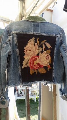 an old jean jacket with embroidered flowers on the back, hanging from a clothes hanger