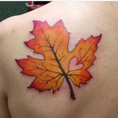 an orange and yellow leaf tattoo on the back of a woman's shoulder,