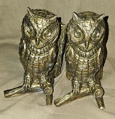 two metal owl figurines sitting on top of a bed