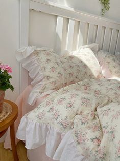 a bed with pink flowers and white ruffles on the sheets, pillows and pillow cases