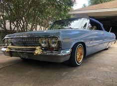 an old blue car parked in front of a house with gold rims on it