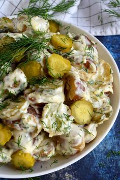 a white bowl filled with potato salad on top of a blue table cloth and green sprigs