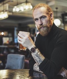 a man sitting at a table with a glass in his hand and tattoos on his arm