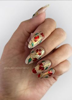 a woman's hand with gold and red flowers on her nails, holding onto the nail