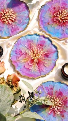 four plates with flowers on them sitting on a table next to some leaves and other things