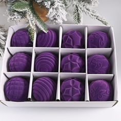 an open box filled with purple cookies on top of a white table next to a christmas tree