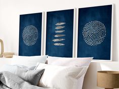 three blue paintings hang on the wall above a bed