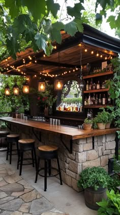 an outdoor bar with stools and lights hanging from it's roof, surrounded by greenery