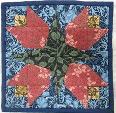 a blue and red quilt with an orange flower on the center, surrounded by leaves