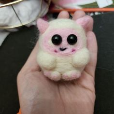 a hand holding a small white and pink stuffed animal