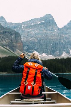 a person in a canoe paddling on the water with mountains in the back ground