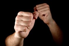 two hands with fists raised up in the air against a black background and one hand holding something