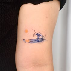 a small wave tattoo on the back of a woman's left arm, with an orange sun in the background