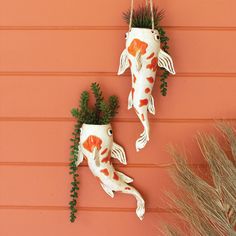 two ceramic fish hanging on the side of a wall next to some plants and grass