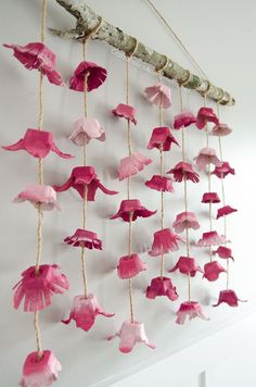 pink paper flowers hanging from a branch on the wall in front of a white wall