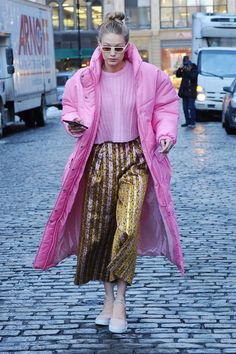 a woman in a pink coat and gold skirt walking down a cobblestone street