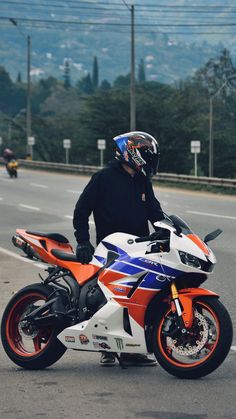 a man in black jacket and helmet sitting on motorcycle next to road with mountains in the background