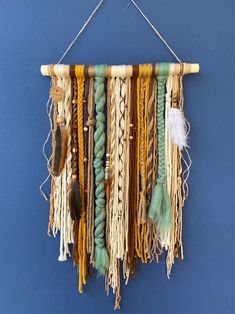 a wall hanging made out of different colored ropes and feathers on a blue wall with a hook