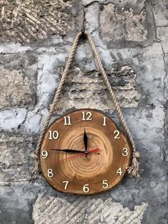 a wooden clock hanging from a rope on a stone wall