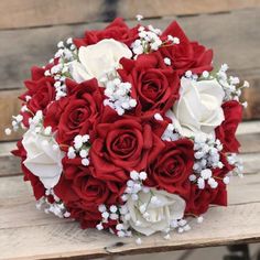 a bridal bouquet with white and red roses on a wooden bench in front of a building