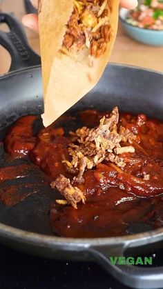 someone is holding up a piece of meat in a skillet with other food items