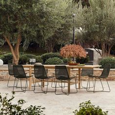 an outdoor dining table with four chairs around it and trees in the backround