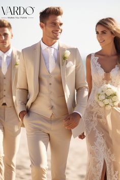 two men and a woman in wedding attire walking on the beach with one man wearing a tuxedo