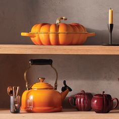 an orange tea kettle sitting on top of a wooden shelf next to other kitchen utensils