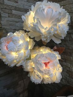 three large white flowers sitting on top of a table next to a brick wall with lights