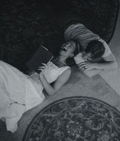 two people are laying on the floor and one is holding a book in her hands