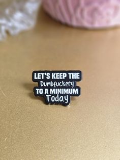 a black and white lapel pin that says, let's keep the dumbbucky to a maximum today