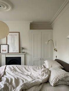 an unmade bed with white sheets and pillows in a bedroom next to a fireplace