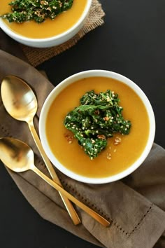 two white bowls filled with soup on top of a brown napkin next to gold spoons