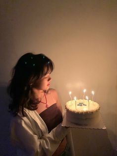 a woman holding a cake with lit candles on it in front of a white wall