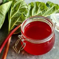 a glass jar filled with red liquid next to some green leafy vegetables on a table