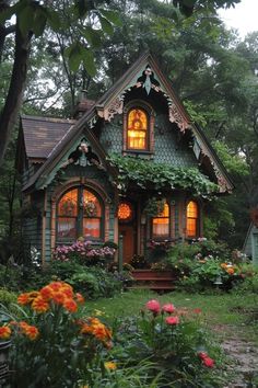 a small house with lots of windows and flowers around it's front door, in the woods