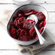 a white bowl filled with beets on top of a table next to a spoon