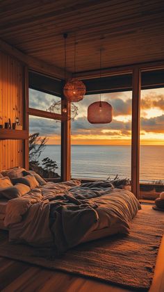 a bedroom with a large window overlooking the ocean at sunset or sunrise, and an unmade bed